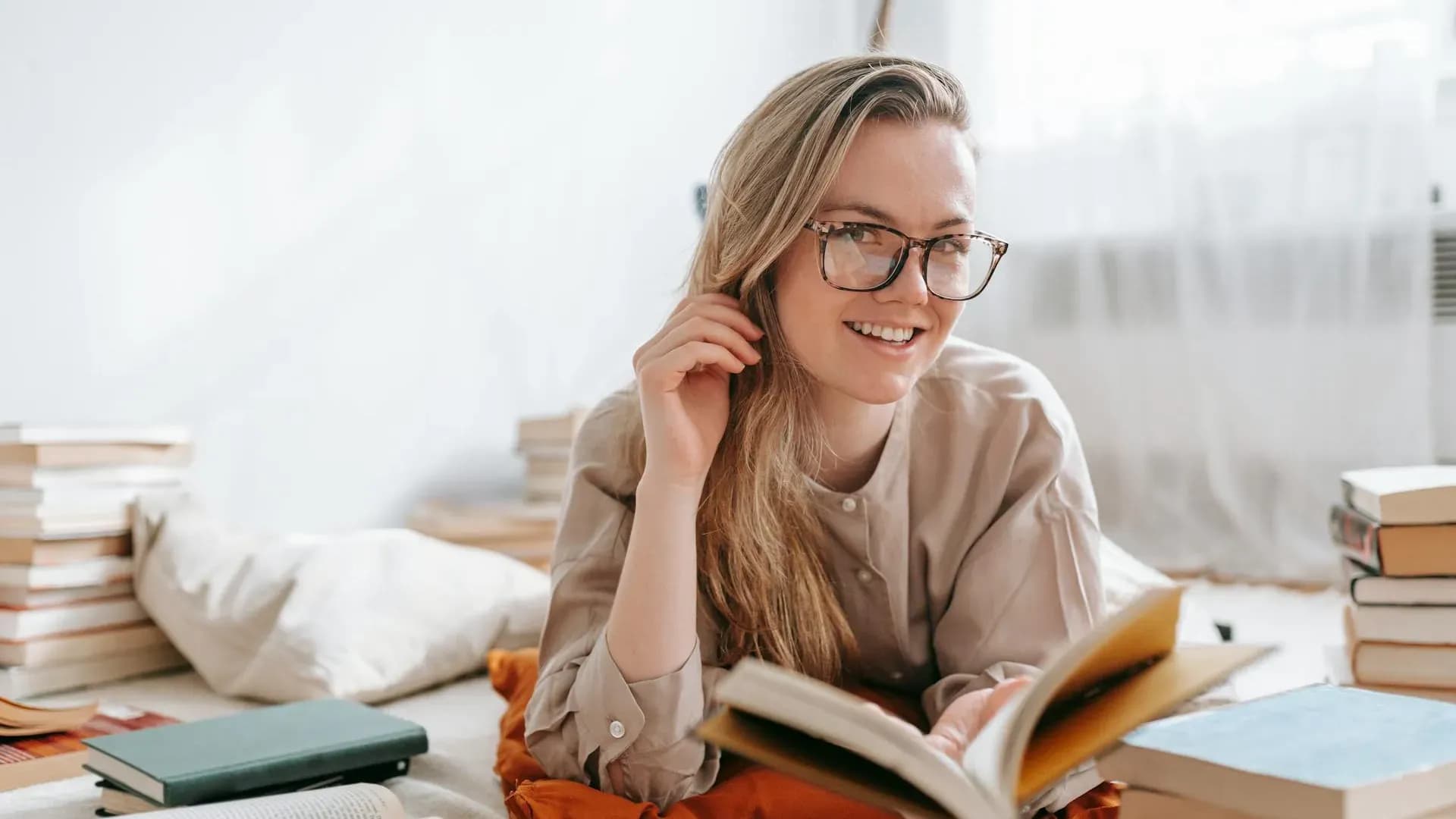 Smiling woman with glasses reading among stacks of books