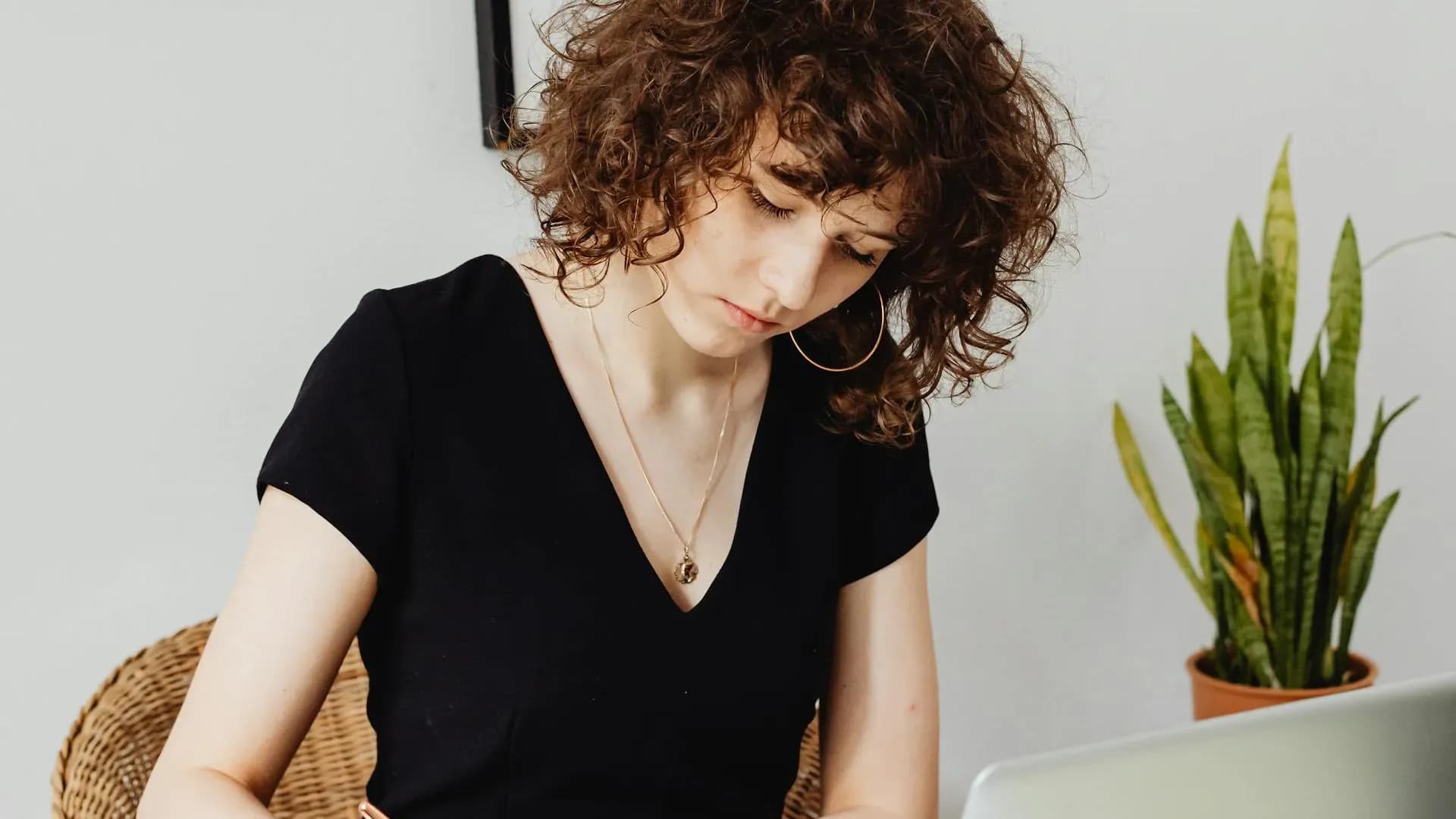 Creative woman with curly hair deep in thought while writing at her desk