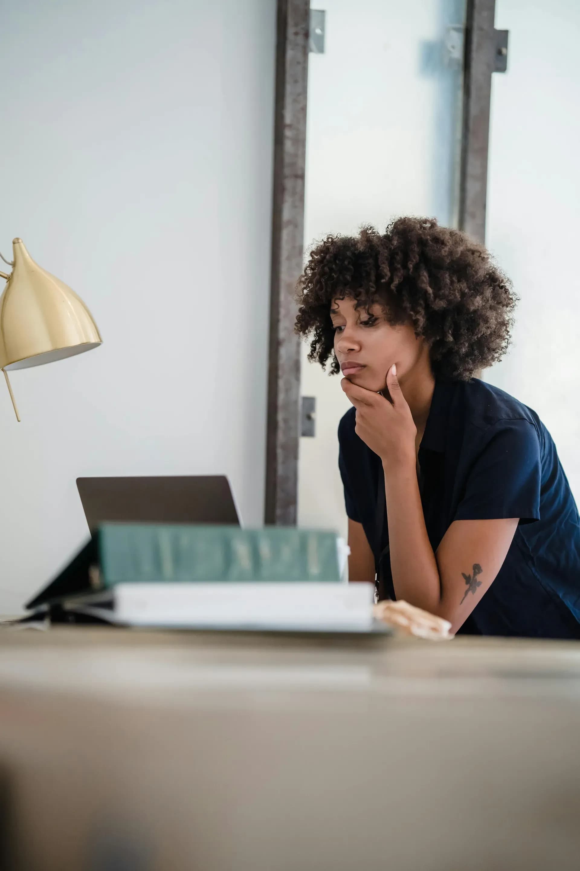 Professional woman at her desk in a modern office, hand on chin in a contemplative expression, reflecting on her next step