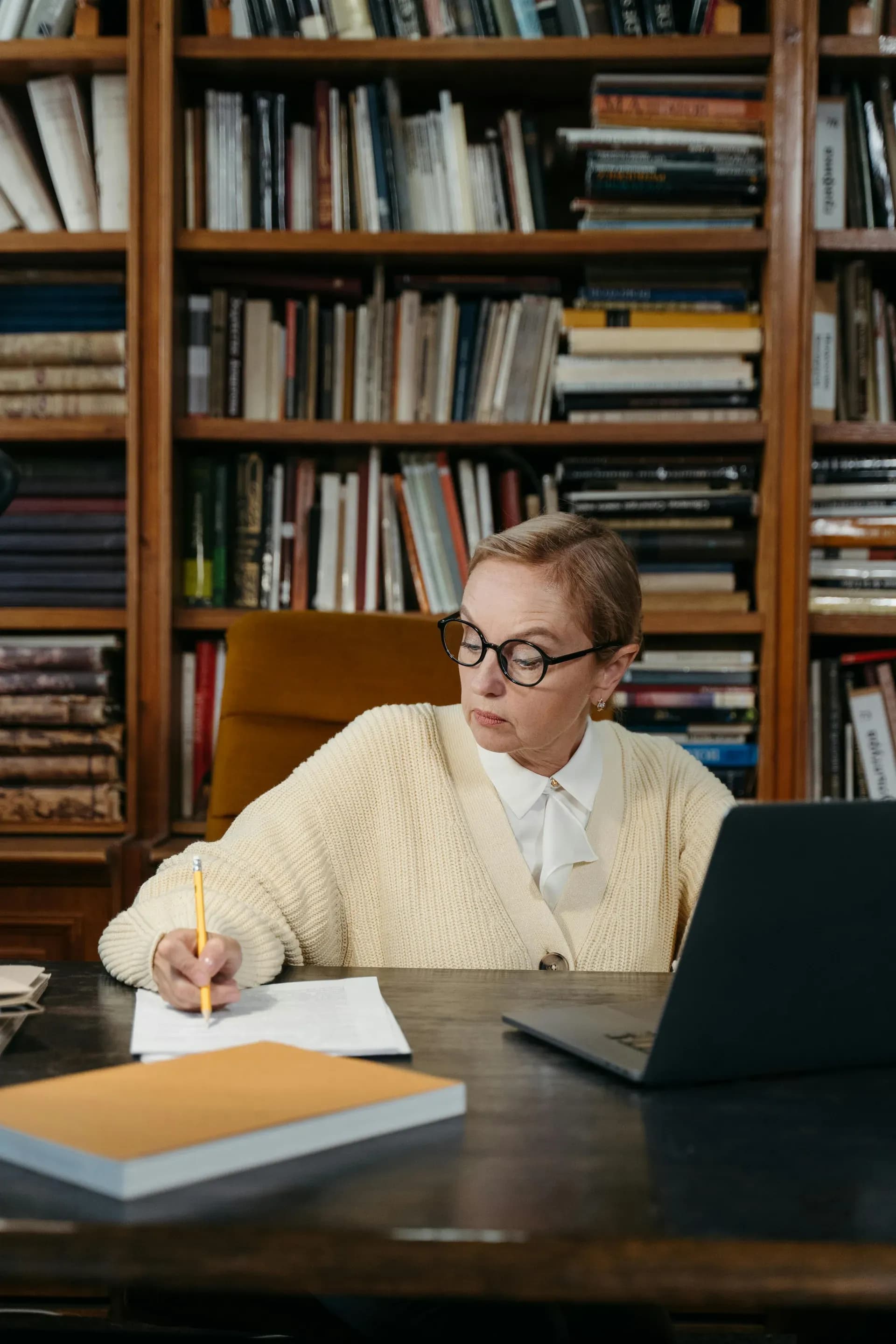 Older woman taking notes at a desk while learning with a laptop