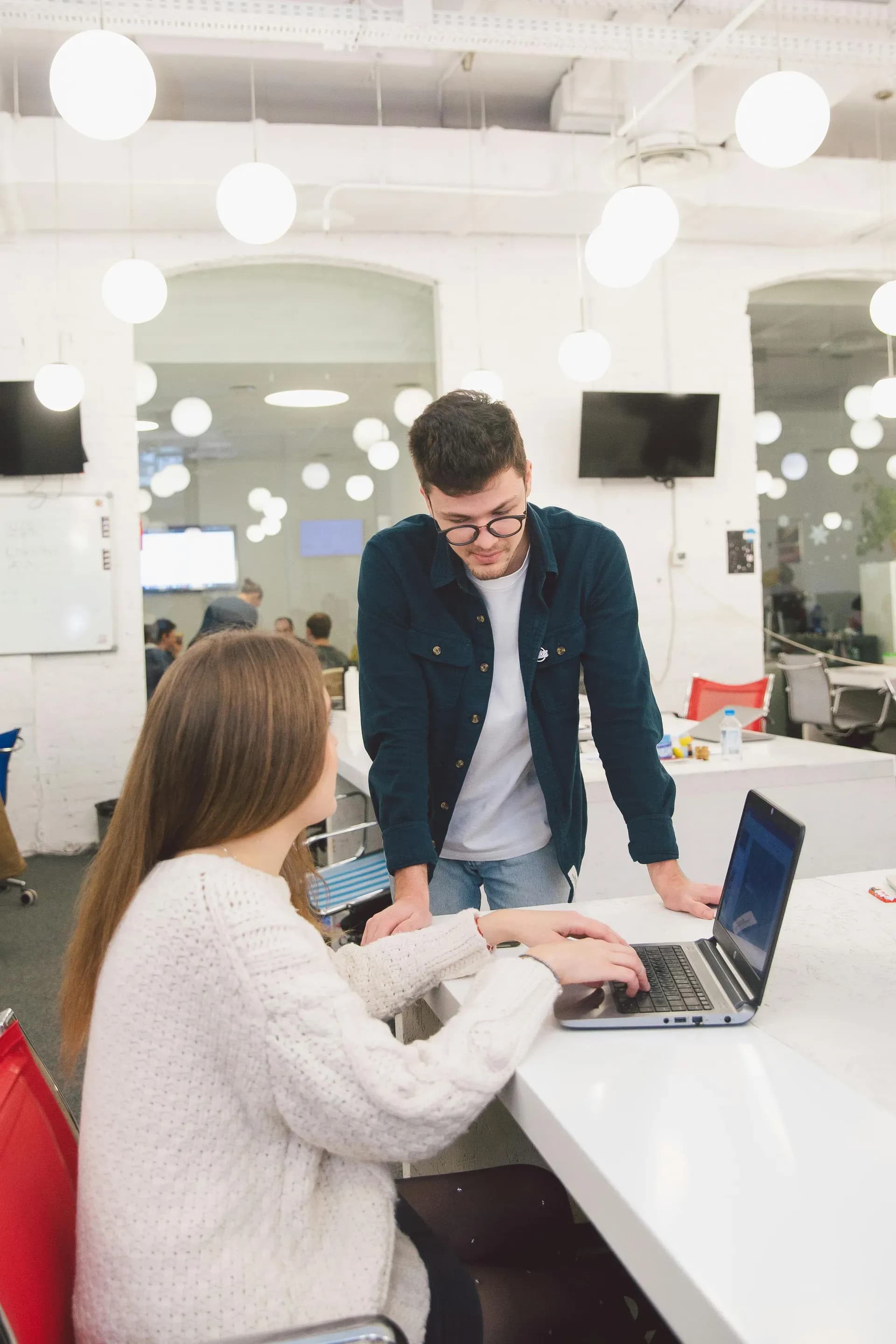 Two colleagues discussing content on a laptop in a bright office, one explaining to the other