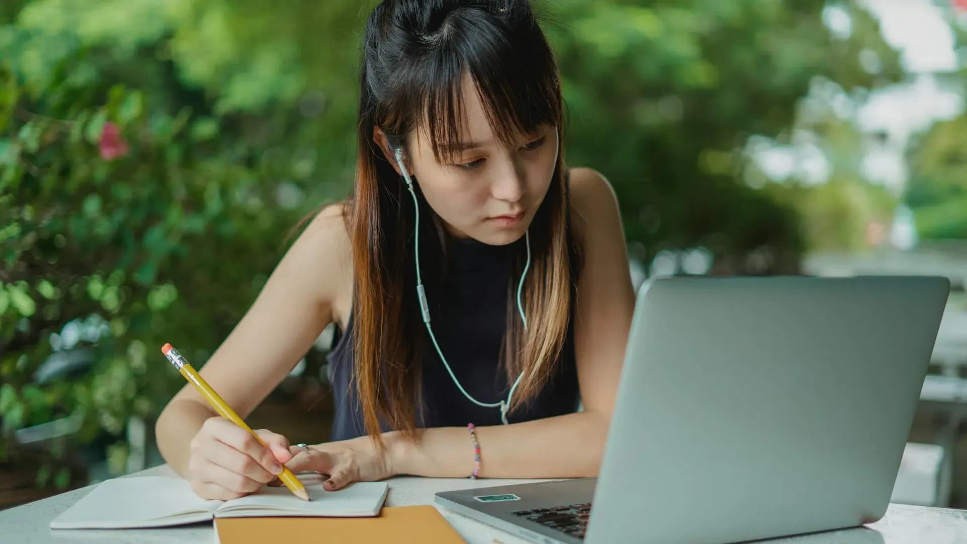 Student taking notes beside a laptop with focused concentration
